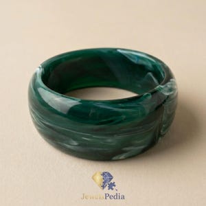 May include: A thick, circular bangle bracelet made of polished resin in a deep forest green colour. The material features a swirling, marbled pattern with translucent white and lighter green streaks throughout the smooth, rounded surface.