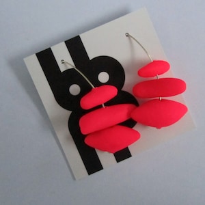 May include: A pair of neon pink dangle earrings with a stacked geometric design. The earrings are made of polymer clay and have silver wire hoops.