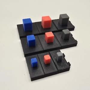 May include: A 3D-printed puzzle game with black platforms and colorful cubes. The cubes are blue, red, and gray, and are arranged on the platforms. The game is likely a brain teaser or a strategy game.