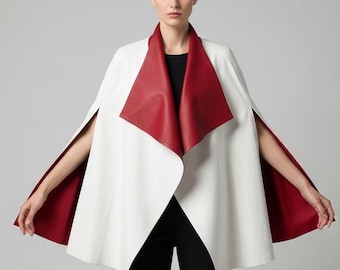 May include: A white cape with a red collar and lining. The cape has a unique design with a wide collar and open sleeves. The model is wearing black pants and a black top. The cape is made of a smooth material.