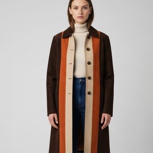 Op de afbeelding: Een lange bruine jas met een verticaal streepontwerp in oranje en beige. De jas heeft een kraag, knoopsluitingen en een getailleerde pasvorm. Het model draagt een crèmekleurige coltrui en een blauwe jeans.