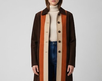 Pode incluir: Um casaco comprido castanho com um design de riscas verticais em laranja e bege. O casaco tem gola, botões e um corte sob medida. A modelo está vestindo uma gola alta creme e jeans azuis.