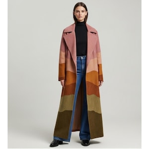 May include: A long, color-blocked coat in shades of pink, orange, and olive green. The coat has a wide lapel and a floor-length design. The model is wearing a black turtleneck and blue jeans. The coat is a statement piece.