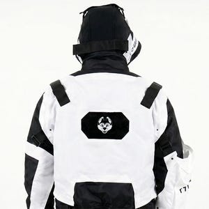 Pu&ograve; includere: Giacca bianca e nera con cappuccio, vista da dietro. La giacca presenta un pannello frontale bianco con un emblema nero e dettagli neri. Il cappuccio &egrave; nero e la giacca sembra essere realizzata in un materiale resistente.