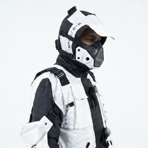 Pu&ograve; includere: Un completo futuristico in bianco e nero, composto da giacca, maschera e berretto. La giacca ha pi&ugrave; tasche e cinghie. Il testo &egrave; visibile sul berretto e sulla maschera. Il completo ha un design urbano moderno.