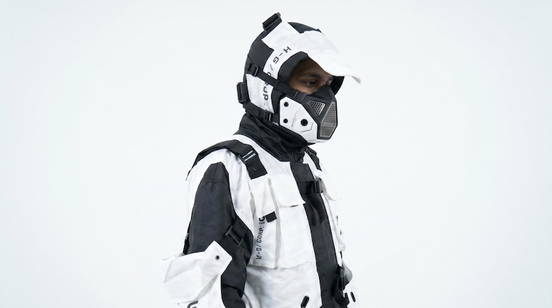 Pu&ograve; includere: Un completo futuristico in bianco e nero, composto da giacca, maschera e berretto. La giacca ha pi&ugrave; tasche e cinghie. Il testo &egrave; visibile sul berretto e sulla maschera. Il completo ha un design urbano moderno.