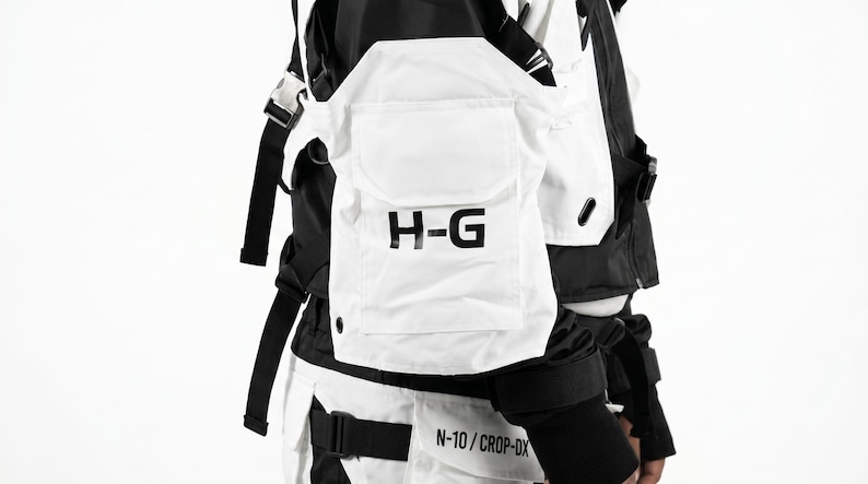 Pu&ograve; includere: Gilet tattico bianco e nero con pi&ugrave; tasche e cinghie. Il gilet presenta le lettere "H-G" stampate in nero su una tasca frontale. Il design include una combinazione di pannelli bianchi e neri, con cinghie e fibbie regolabili.