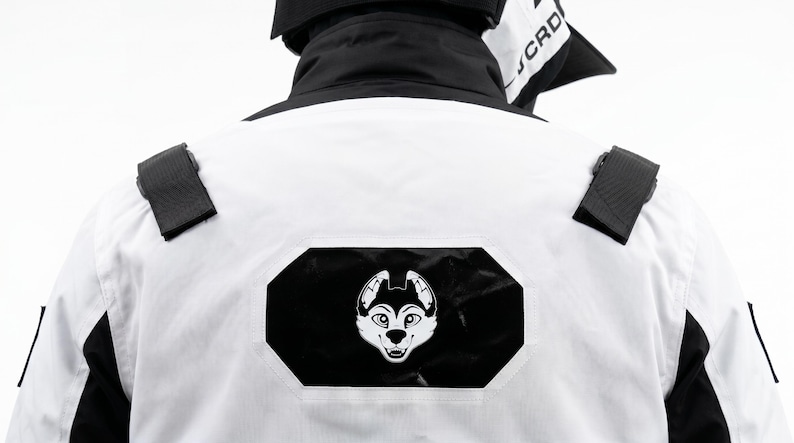 Pu&ograve; includere: Giacca bianca e nera con logo a forma di muso di husky bianco e nero sul retro. La giacca presenta dettagli neri e cinturini neri sulle spalle. Il colletto &egrave; nero e il capo sembra essere realizzato in un materiale resistente.