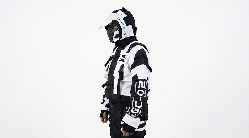 Pu&ograve; includere: Un completo futuristico in bianco e nero con casco, maschera facciale e giacca. La giacca ha pi&ugrave; tasche e il testo "GC-02" sulla manica. Il completo &egrave; progettato con un'estetica moderna e tecnica.
