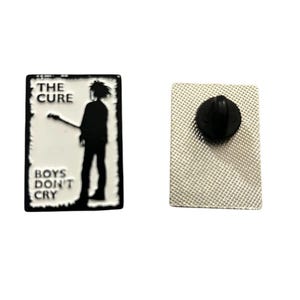 May include: Two rectangular enamel pins. One pin features a black and white graphic of a person holding a guitar with the text "THE CURE" and "BOYS DON'T CRY". The other pin has a black pin back.