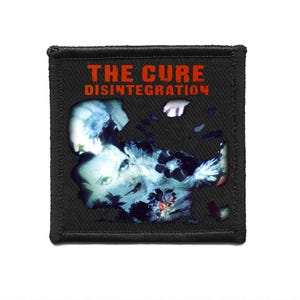 May include: Black square patch featuring the text "THE CURE DISINTEGRATION" in orange. The patch has a blue and white graphic design of a face and floral elements.