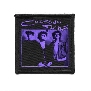 May include: A black patch featuring a purple image of the band Cocteau Twins. The image shows three band members in a purple hue. The band's name is written in purple script at the top of the patch.
