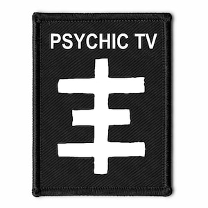 Puede incluir: Parche rectangular negro con texto blanco "PSYCHIC TV" sobre un símbolo blanco. El símbolo es una cruz estilizada. El parche tiene un borde negro.
