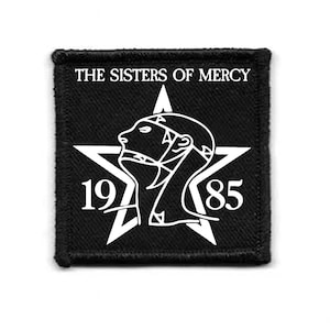 Può includere: Toppa quadrata nera con la scritta "THE SISTERS OF MERCY" sopra una stella bianca e un profilo stilizzato. I numeri "197" e "85" sono sotto. La toppa ha un bordo nero.