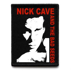 May include: Black embroidered patch with a white and black portrait. The red text "NICK CAVE" is at the top, and "AND THE BAD SEEDS" is in red vertically on the right. The patch has a black border and is likely for clothing or accessories.