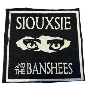 May include: Black and white patch featuring the band name "Siouxsie and the Banshees" with stylized eyes. The text and graphic are in white against a black background, framed by a white border.
