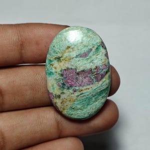 May include: An oval-shaped cabochon gemstone featuring a marbled texture with a mix of vibrant mint green, creamy white, and deep magenta-pink inclusions. The surface has a polished, smooth finish with visible natural mineral veining throughout.