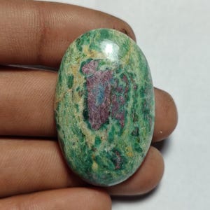 May include: An oval gemstone displaying a blend of green, red, and blue shades. The polished surface reveals a natural pattern of colours and textures. This gemstone is likely intended for jewellery or decorative applications.