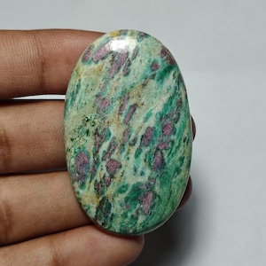 May include: An oval-shaped cabochon gemstone featuring a polished surface with a marbled pattern of vibrant green, cream, and deep magenta-pink inclusions. The stone displays a smooth, rounded top and a glossy finish throughout its entire surface.
