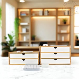 以下が含まれることがあります： 白い引き出しが付いた2つの竹製デスクオーガナイザー。1つは2つの引き出しがあり、もう1つは3つあります。小さな透明な容器と灰色のキーボードがオーガナイザーの前にあります。背景には木製の本棚があります。