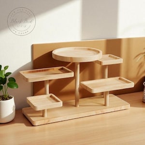 May include: A multi-tiered, light-colored wooden display stand with a circular top and several rectangular and square shelves. The stand is designed to showcase small items and has a natural wood finish. The text "FROM OUR NEST Black Bird & Sky TO YOURS" is in a circle in the upper left corner.