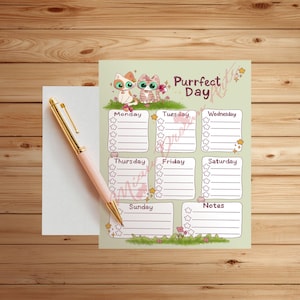 Könnte beinhalten: Ein rosa-goldener Stift liegt auf einem weißen Notizblock neben einem Wochenplaner. Der Planer hat einen grünen Hintergrund mit Cartoon-Katzen, dem Text "Purrfect Day" und täglichen Abschnitten.