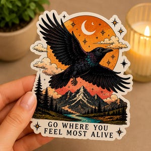 May include: A sticker featuring a black raven in flight against a sunset backdrop with mountains and a river. The design includes the text "GO WHERE YOU FEEL MOST ALIVE" and stars.