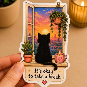 May include: A die-cut sticker featuring a black cat sitting on a windowsill looking out at a sunset over a city. The scene includes a hanging plant, a potted plant, and a pink mug with a heart. The text reads, It's okay to take a break.