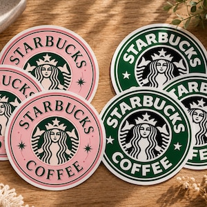 May include: A collection of round Starbucks coffee coasters. The coasters feature the Starbucks logo with a green and pink color scheme. The logo includes the Starbucks siren and the words "STARBUCKS COFFEE".