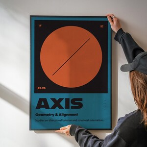 May include: A framed poster with a geometric design. The poster features a large orange circle bisected by a diagonal black line against a black background. Below, the word "AXIS" is displayed in bold, black letters above the text "Geometry & Alignment".