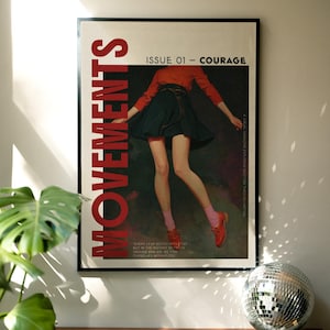 May include: A framed poster with the word "MOVEMENTS" in large red letters. The poster features an illustration of a person in a red top and dark skirt. Text reads "ISSUE 01 - COURAGE". A disco ball sits on a wooden surface.