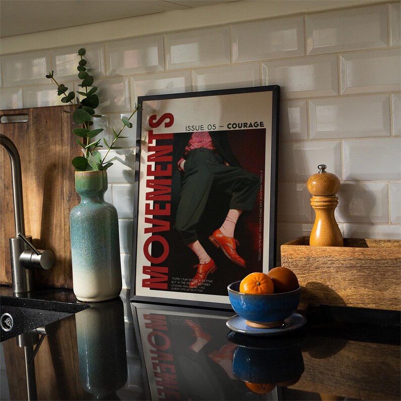May include: A kitchen scene featuring a framed poster with the word "MOVEMENTS" in red, and the text "ISSUE 05 - COURAGE". A blue and white vase holds greenery. A wooden cutting board and a wooden box with a pepper grinder are also visible.