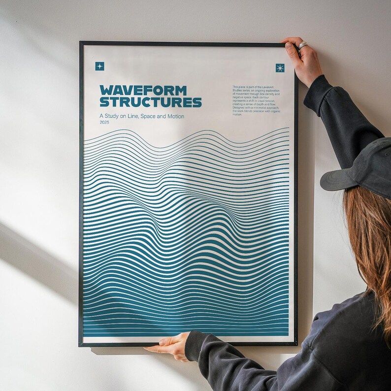 May include: A framed art print titled "WAVEFORM STRUCTURES" with teal and white wavy lines. The text "A Study on Line, Space and Motion" is below the title. The print is held by a person wearing a black cap and a black long-sleeve shirt.