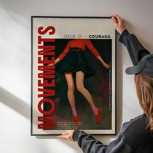 May include: A framed poster with the word "MOVEMENTS" in large red letters. The poster features an illustration of a person in a red top and dark skirt. Text reads "ISSUE 01 - COURAGE" and "A VISUAL MAGAZINE EXPLORING EMOTION THROUGH MOTION."