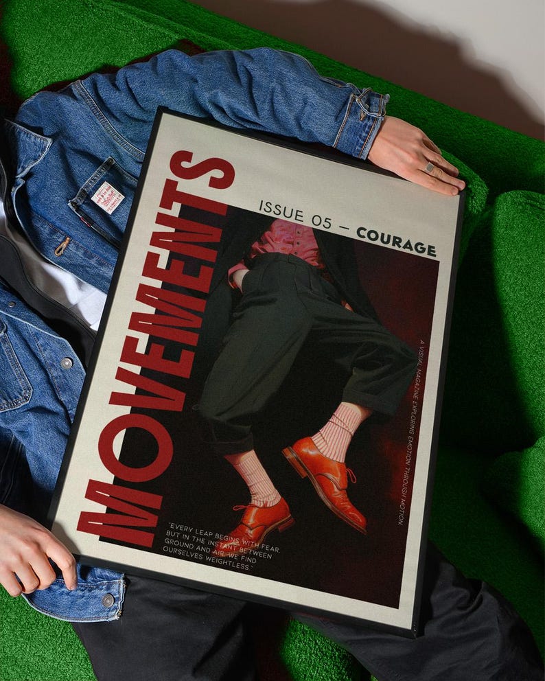 May include: A framed magazine cover with the title "MOVEMENTS" in large red letters. The cover features an image of a person wearing orange shoes and black pants. The text "ISSUE 05 - COURAGE" is also visible. The magazine is held by a person wearing a denim jacket.