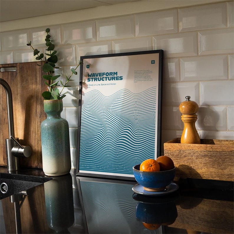 May include: A framed poster with the text "WAVEFORM STRUCTURES" and a blue and white wave design. A blue ceramic bowl with oranges sits on a black countertop. A green and white vase holds greenery. A wooden pepper grinder and a wooden box are also visible.