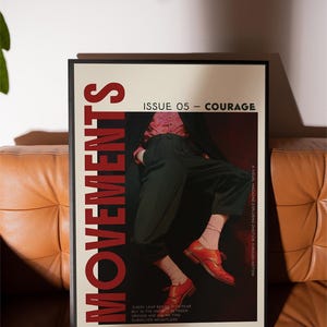 May include: A framed poster with the word "MOVEMENTS" in large red letters. The poster features a person in black pants and red shoes. The text "ISSUE 05 - COURAGE" is at the top. The poster is on a brown leather couch.