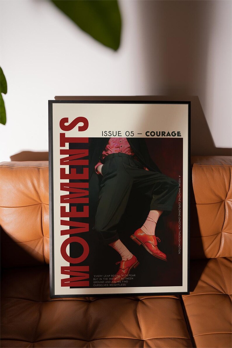 May include: A framed poster with the word "MOVEMENTS" in large red letters. The poster features a person in black pants and red shoes. The text "ISSUE 05 - COURAGE" is at the top. The poster is on a brown leather couch.