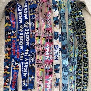 May include: A selection of vibrant lanyards showcasing cartoon characters. Designs include Mickey Mouse, Minnie Mouse, and Stitch, with text such as "MICKEY" and "MINNIE". The lanyards have metal clasps and are suitable for holding keys or ID badges.