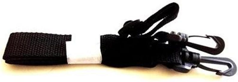 May include: Black nylon strap with two black plastic clips. The strap has a white section in the middle and is folded over on the left side. The clips are attached to a black section of the strap.