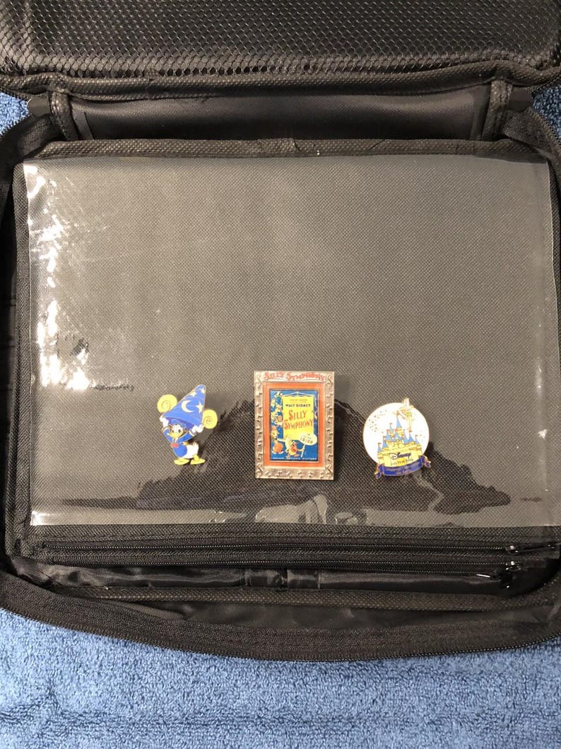 May include: Black zippered carrying case with clear plastic sleeves, holding three Disney pins. The pins feature cartoon characters and scenes, including a Sorcerer Mickey Mouse, a framed "Silly Symphonies" pin, and a castle design.