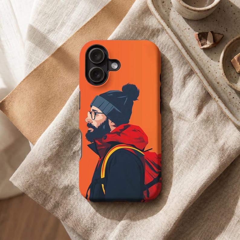 Peut inclure: Coque de t&eacute;l&eacute;phone orange avec une illustration stylis&eacute;e d'une personne avec une barbe, des lunettes et un bonnet. La personne porte une veste rouge et un sac &agrave; dos. La coque a un appareil photo &agrave; double objectif.