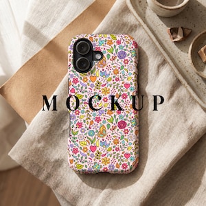 Peut inclure: Une coque de t&eacute;l&eacute;phone avec un motif floral color&eacute;, comprenant des fleurs, des c&oelig;urs et des papillons. Le fond de la coque est rose et le mot "MOCKUP" est imprim&eacute; en noir. La coque est pos&eacute;e sur une surface de couleur neutre.