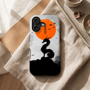 Peut inclure: Coque de t&eacute;l&eacute;phone avec une silhouette noire de dragon sur un paysage rocheux, sur fond de soleil orange. Le design comprend des oiseaux en vol et une esth&eacute;tique minimaliste.