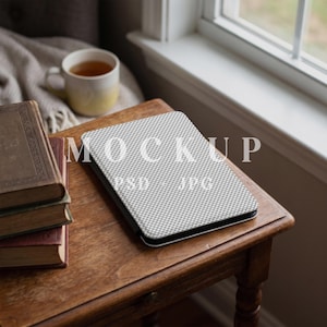 May include: A rectangular tablet case with a white and grey chequered pattern, featuring the text MOCKUP PSD + JPG printed on the surface. The case is positioned on a wooden table next to a stack of three vintage books and a ceramic mug.