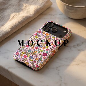 May include: A light pink phone case adorned with a vibrant floral pattern featuring flowers, hearts, and butterflies. The case has a black camera section and the word "MOCKUP" is printed on the case.