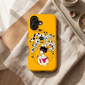 Peut inclure: Coque de t&eacute;l&eacute;phone jaune vif avec une illustration de femme entour&eacute;e d'animaux de dessin anim&eacute;. La femme porte un haut rose et des boucles d'oreilles dor&eacute;es. Le bo&icirc;tier est dot&eacute; d'un appareil photo &agrave; double objectif.