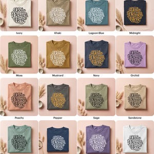 May include: A collection of folded t-shirts in various colors, including ivory, khaki, and lagoon blue. Each shirt features the text "Your Design Here" in a decorative font. The shirts are arranged on a neutral background with decorative elements.