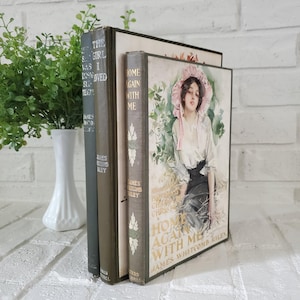 May include: Three vintage books with dark spines and a front cover illustration of a person wearing a pink bonnet and white blouse. The titles include Home Again With Me and The Girl I Loved by James Whitcomb Riley, with gold lettering.