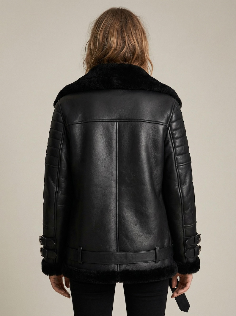 May include: A black leather jacket with a shearling collar and lining. The jacket features a belted waist, buckle details on the sleeves, and quilted shoulder panels. The back view showcases the jacket's design.